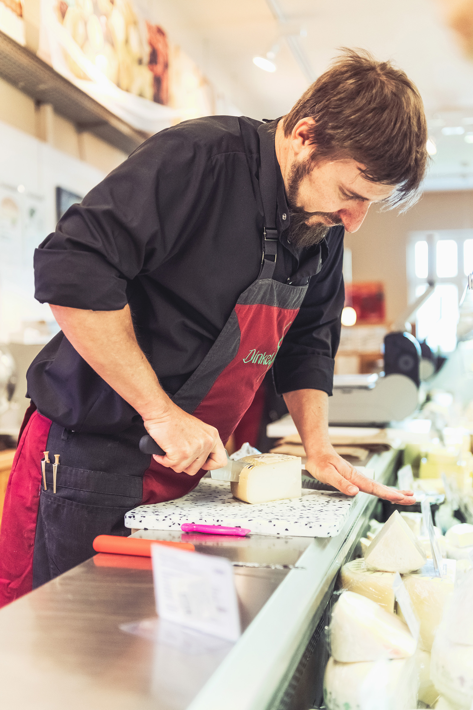 Mann mit Hemd und Latzschürze schneidet Käse im Lebensmitteleinzelhandel